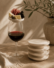 Charcuterie Wine Plates are round whitewashed wooden wine glass toppers, with one holding cheese, salami and olives