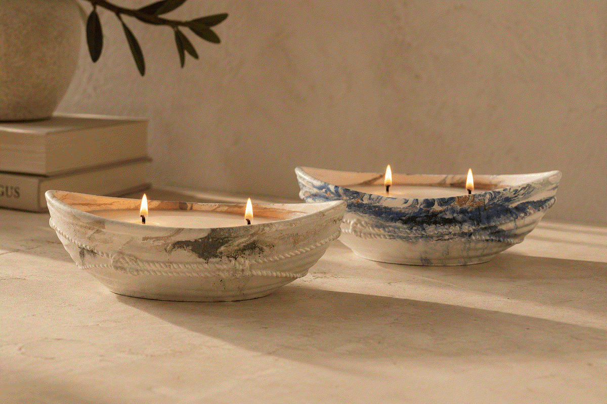 Naus Concrete Candle boat-shaped concrete vessels in natural beige and blue marbled finishes, each holding two lit wicks