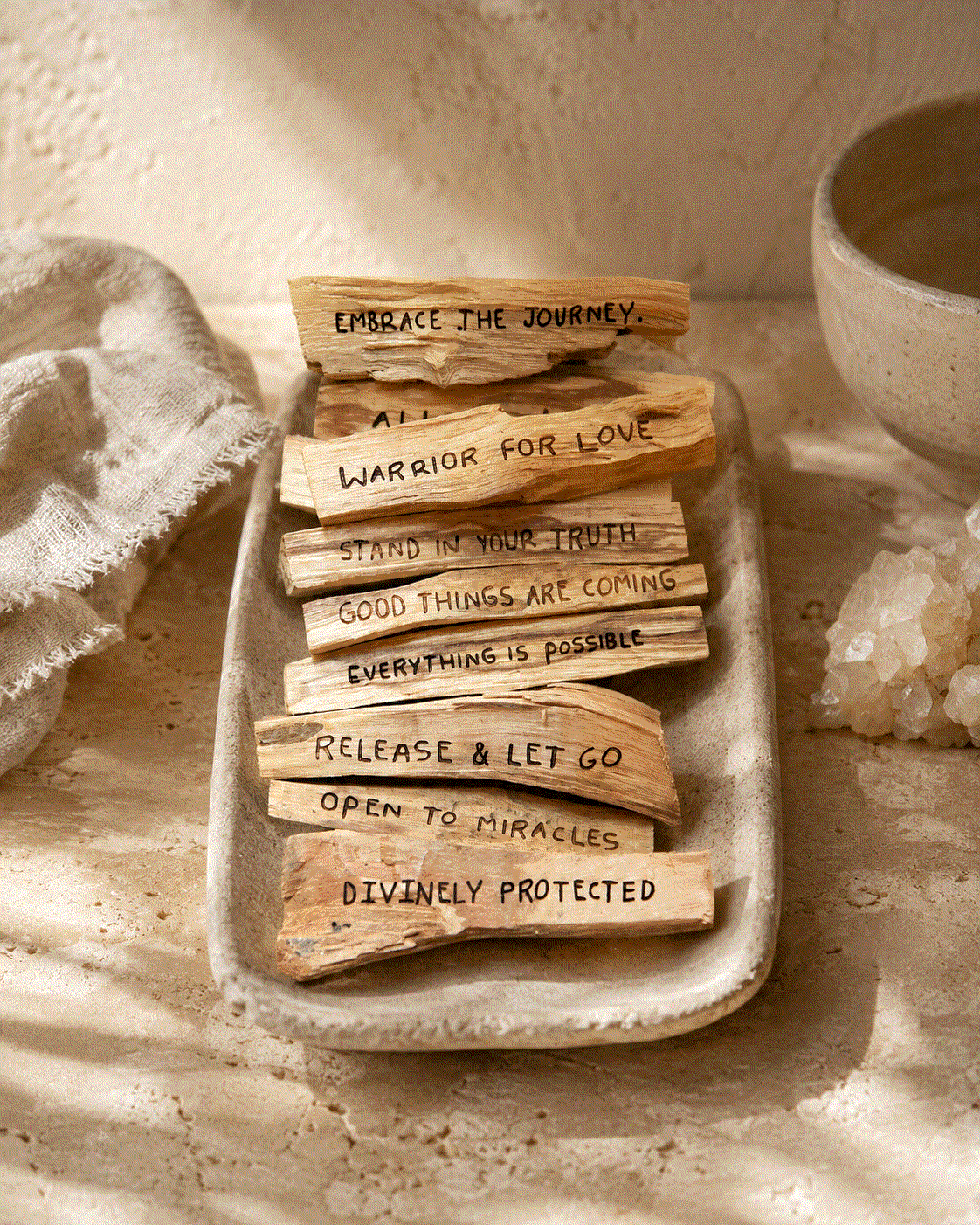 Palo Santo Mantra Sticks are natural light-brown wood pieces with rough grain, each marked with a different affirmation.