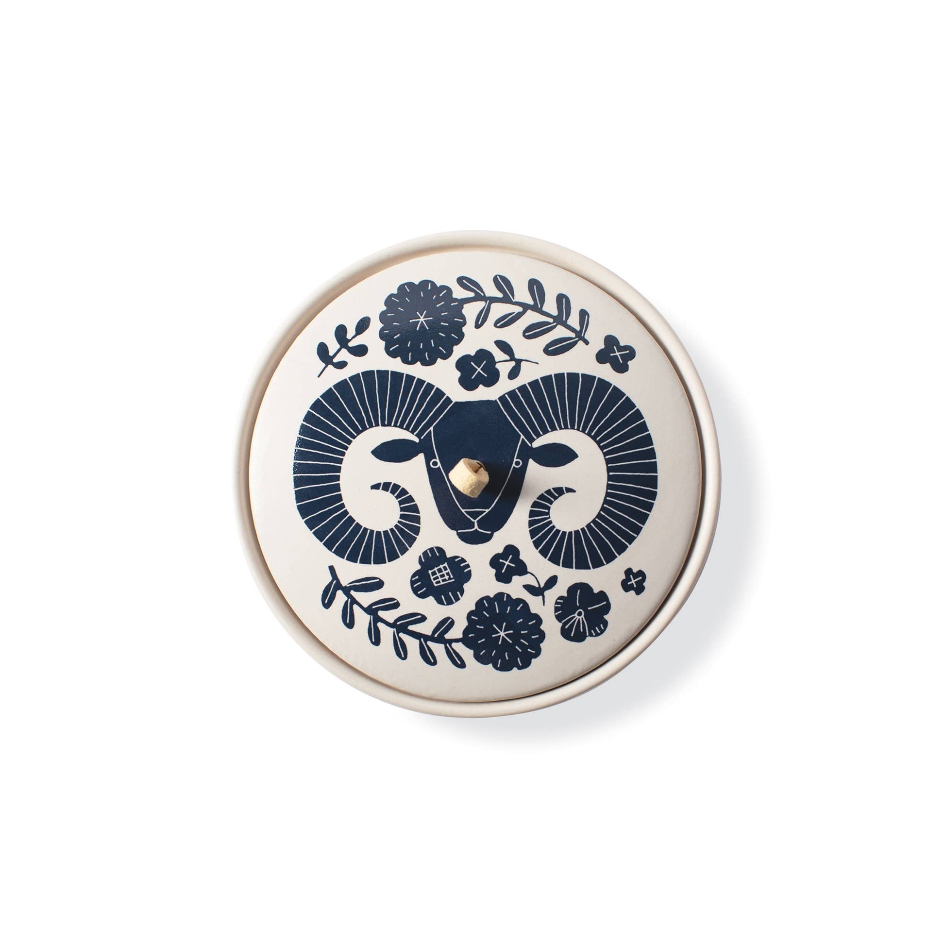 The Rooted Home Aries zodiac ceramic trinket box with a matte cream finish, navy ram illustration, and suede loop.