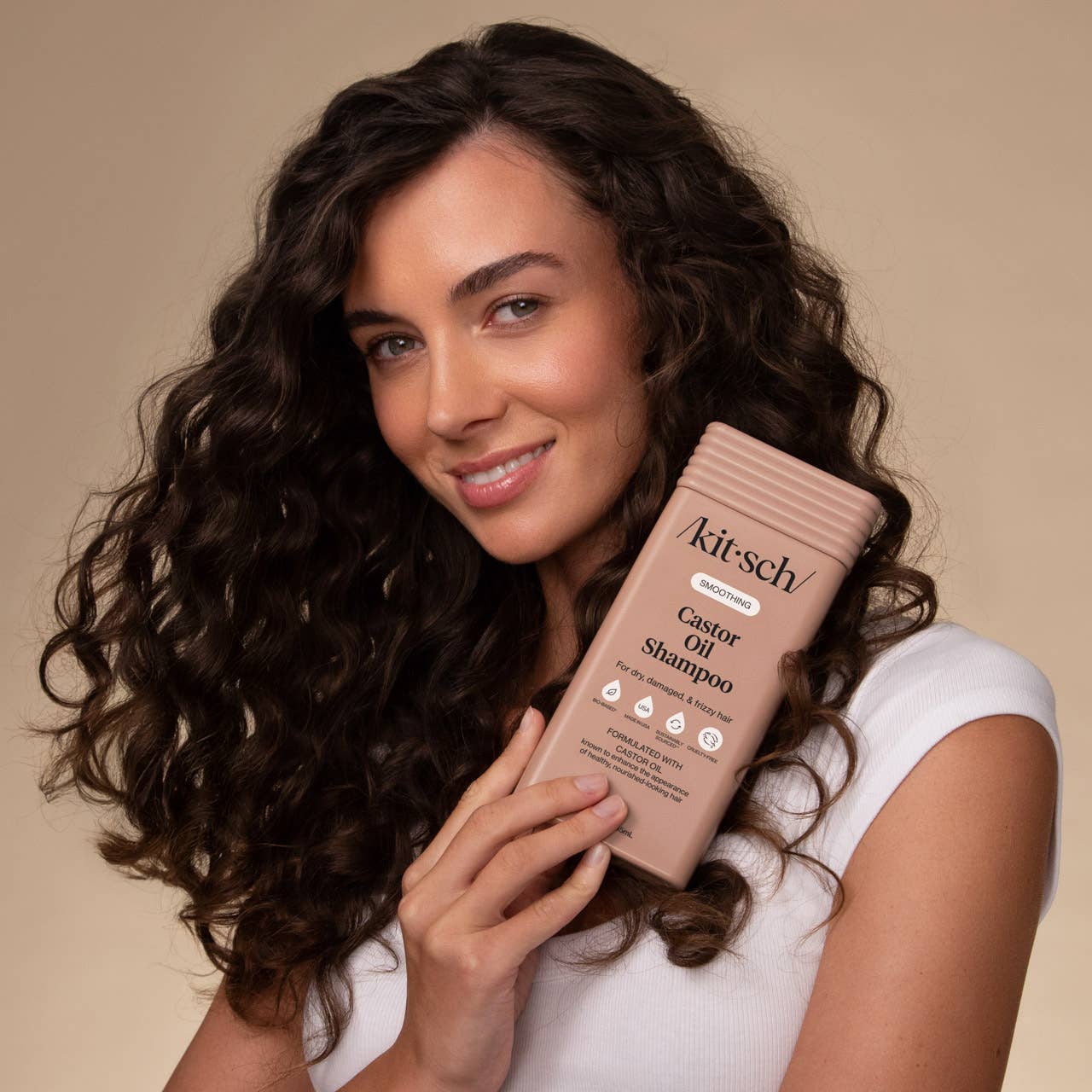 The Rooted Home model holding a bottle of Kitsch Smoothing Castor Oil Shampoo for frizzy hair against a beige background