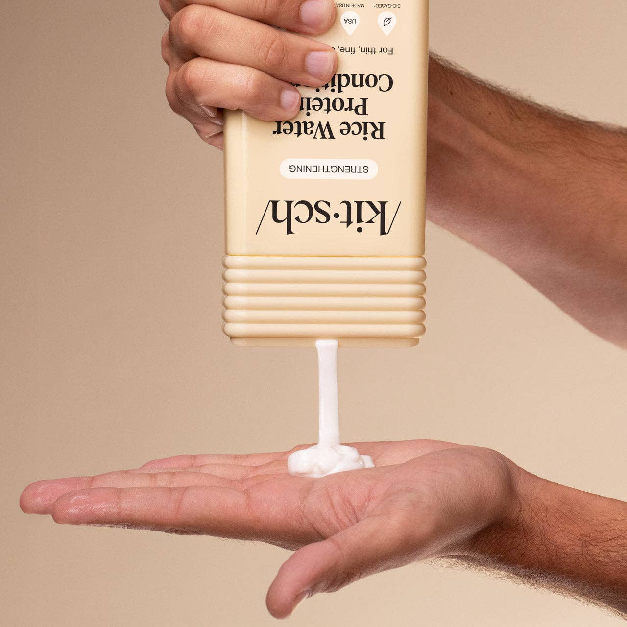 The Rooted Home Kitsch strengthening rice water conditioner being squeezed from a beige bottle into a palm