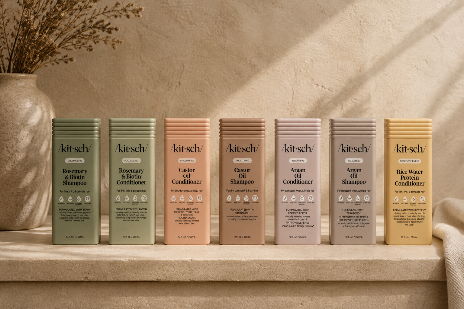 The Rooted Home Kitsch shampoo and conditioner bottles in various pastel colors arranged on a neutral stone shelf.