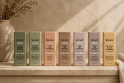 The Rooted Home Kitsch shampoo and conditioner bottles in various pastel colors arranged on a neutral stone shelf.