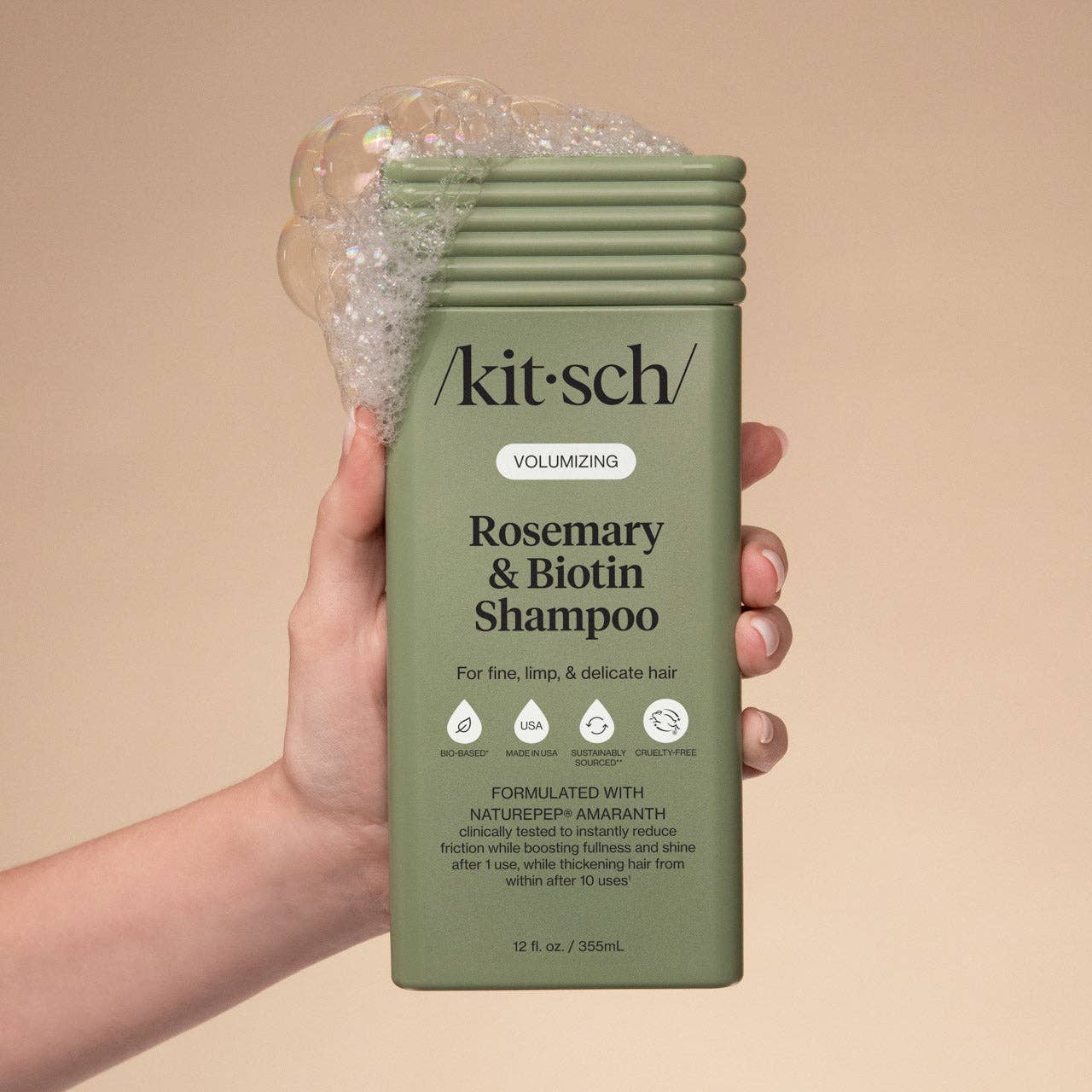 The Rooted Home Kitsch Volumizing Rosemary and Biotin Shampoo bottle held in hand with soap bubbles on top.