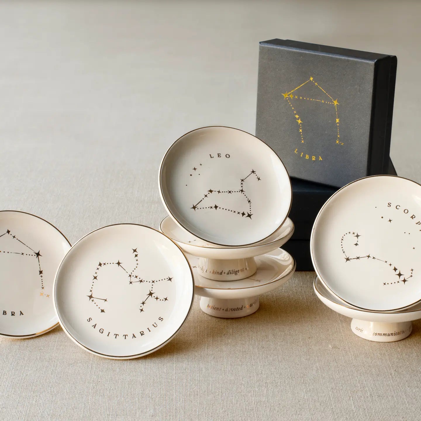 The Rooted Home Zodiac Pedestal Trays in stoneware with gold foil constellation illustrations and gift box