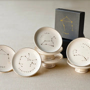 The Rooted Home Zodiac Pedestal Trays in stoneware with gold foil constellation illustrations and gift box