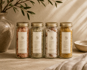 WildFlora Bath Salts in four clear glass jars with gold lids, showing pink, green, cream and yellow mineral blends